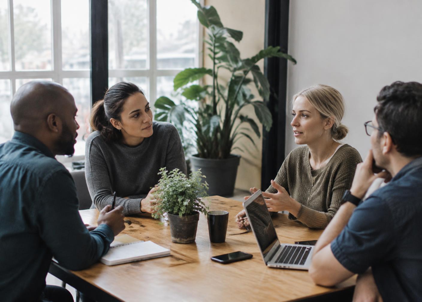 Colleagues in a focused conversation around a wooden table in a bright meeting room